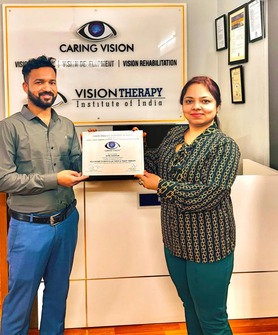 Optom. Sunil receiving Fellowship certificate at Caring Vision branded clinic backdrop